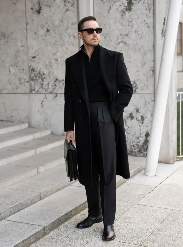 17 Winter Formal Outfits for Men That Look Sharp 9 a man in an All-Black Overcoat with Pleated Trousers and Chelsea Boots